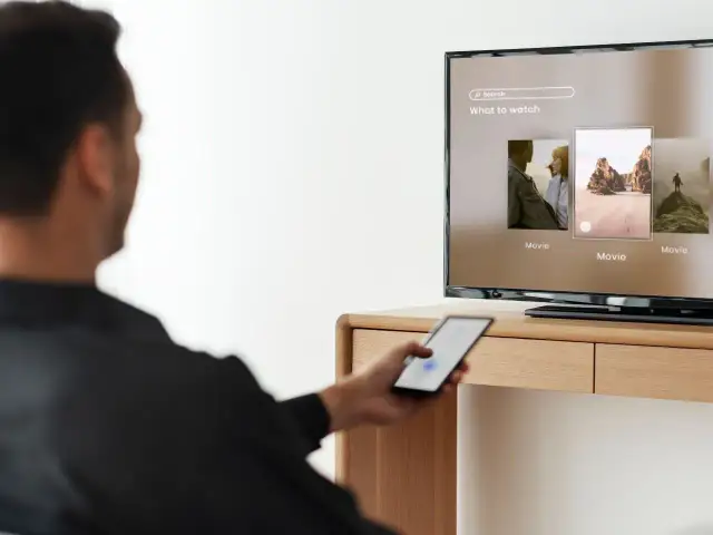 Mężczyzna steruje telefonem, by dowiedzieć się, jak udostępnić internet z telefonu na telewizor i oglądać filmy.