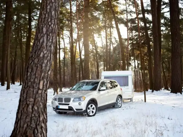 Biały SUV z przyczepą kempingową w zimowym lesie. Idealne warunki do podróży z prawem jazdy B+E.