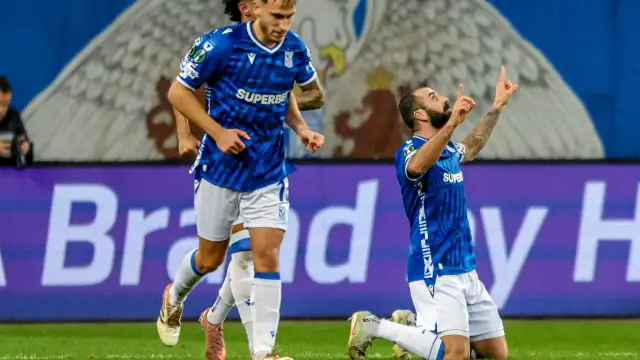 Piłkarz klęczy na boisku, celebrując bramkę. W tle biegnie kolega z drużyny. Wszyscy w niebieskich strojach. Czekamy, kiedy wraca ekstraklasa!