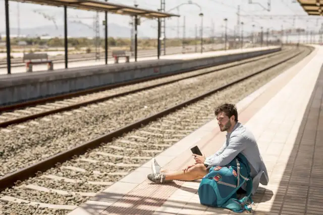 Mężczyzna siedzi na peronie, trzymając telefon. Spóźniłem się na pociąg, co z biletem?