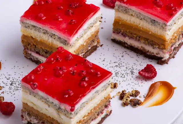 Kawałki wielowarstwowego ciasta z galaretką z czerwonych porzeczek, makiem i kremem.
