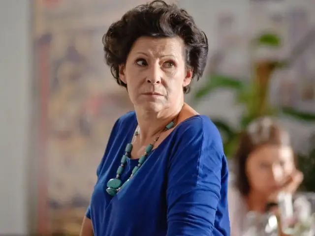 Elegancka polska aktorka po 60. z charakterystyczną fryzurą i turkusowym naszyjnikiem, wpatrzona w dal.