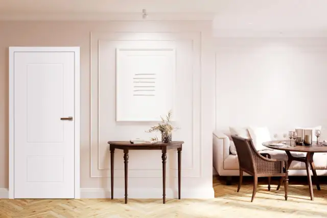 Białe drzwi rewersyjne, konsola z obrazem i wazonem, sofa i stół w jadalni.
