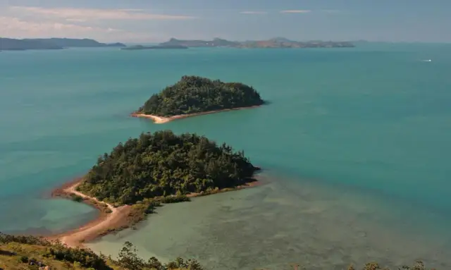 Dwie zielone wyspy porośnięte drzewami na turkusowym morzu, z widokiem na dalsze wyspy w oddali.