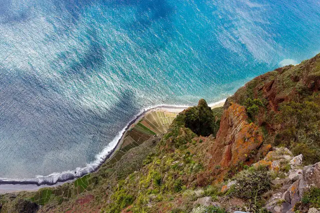 Widok z góry na klif i ocean. Tarasowe pola uprawne na zboczu, fale rozbijające się o brzeg. Madera pogoda styczeń.