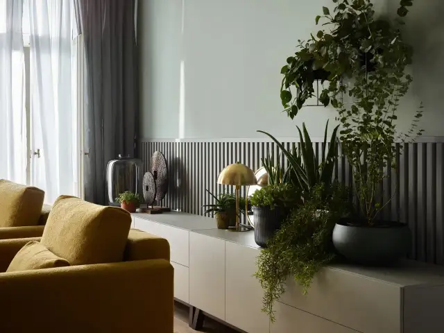 Szare ściany z czym łączyć? Z żółtymi meblami i mnóstwem zieleni. Wnętrze z nowoczesną komodą, lampką i roślinami.