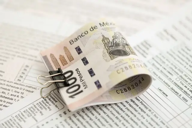 Złożony banknot 100 pesos, przytrzymany spinaczem, leży na dokumentach podatkowych. To pokazuje, co to jest lokata bankowa – sposób na bezpieczne przechowywanie pieniędzy.
