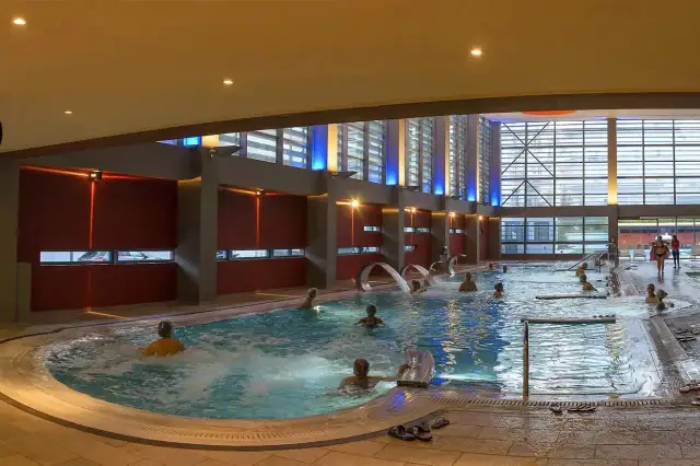 Ludzie relaksują się w basenie termalnym z hydromasażem. Czy na termach trzeba mieć czepek? Tutaj nie widać żadnych czepków.