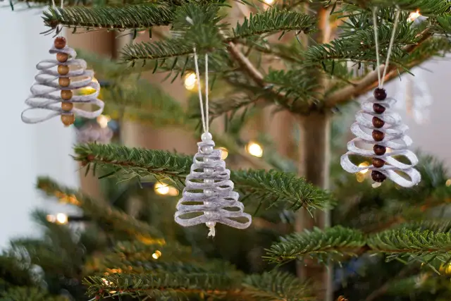 Trzy ręcznie robione ozdoby choinkowe w kształcie drzewek wiszą na gałęziach choinki.