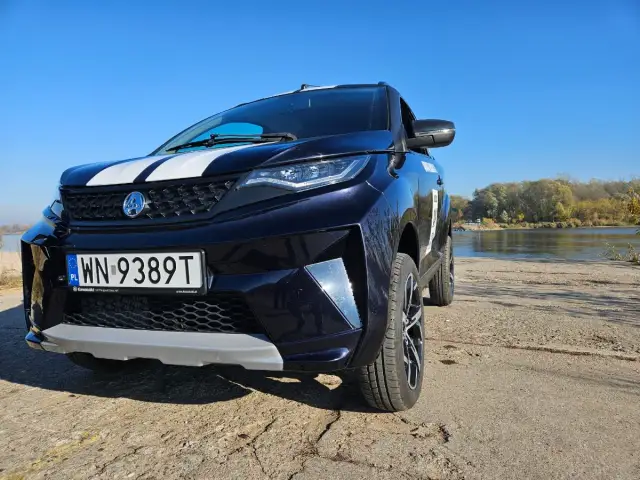 Ciemnoniebieski SUV z białymi pasami na masce, zaparkowany nad rzeką. To auto od 14 lat, gotowe na przygodę.