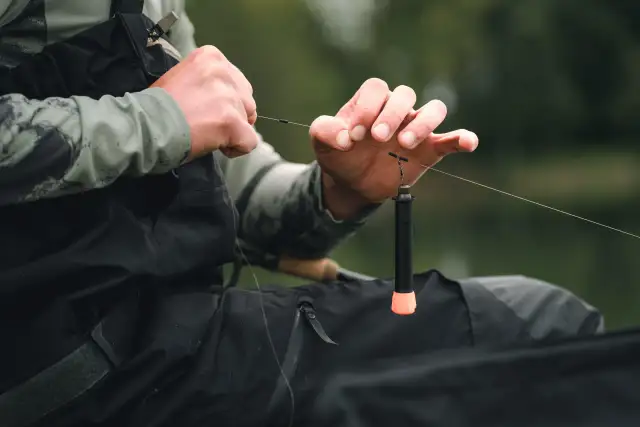 Wędkarz pokazuje, jak założyć spławik na wędkę, precyzyjnie mocując go do żyłki.