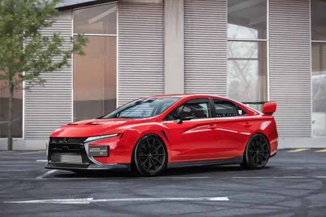 Czerwony Mitsubishi Lancer Evolution XI z czarnymi felgami i spoilerem, zaparkowany przed nowoczesnym budynkiem.
