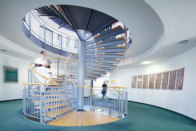 Moderne Wendeltreppe in einer Klinik mit zwei Personen, die sie benutzen.