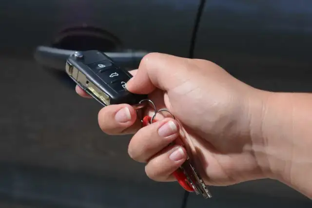 Dłoń trzymająca kluczyk samochodowy z pilotem i pękiem kluczy przy drzwiach samochodu.