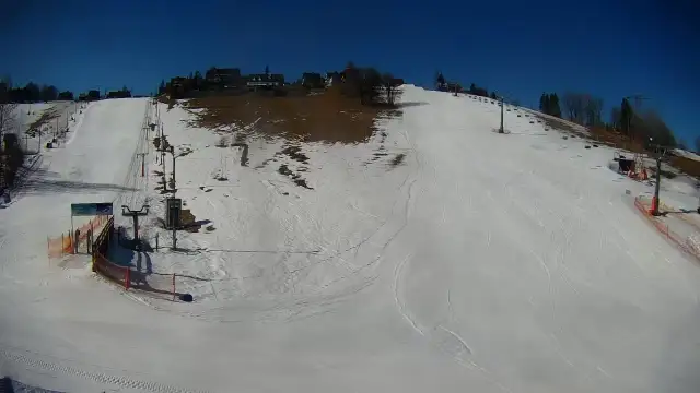 Słoneczny dzień na olczańskim wierchu. Stoki narciarskie, kolejka krzesełkowa i kilka budynków na szczycie.