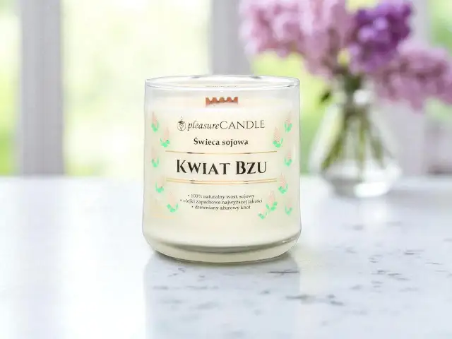 Szklana świeca zapachowa "Kwiat Bzu" z drewnianym knotem, na tle rozmytych kwiatów bzu.