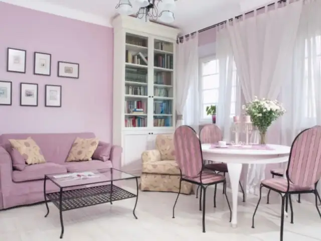 Jasny salon z fioletową kanapą i krzesłami w różowe pasy. Kolor lawendowy ścian świetnie komponuje się z bielą mebli i zasłon, tworząc przytulną atmosferę.