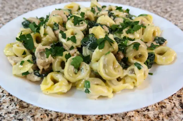 Tortellini ze szpinakiem i kurczakiem w kremowym sosie, posypane natką pietruszki.