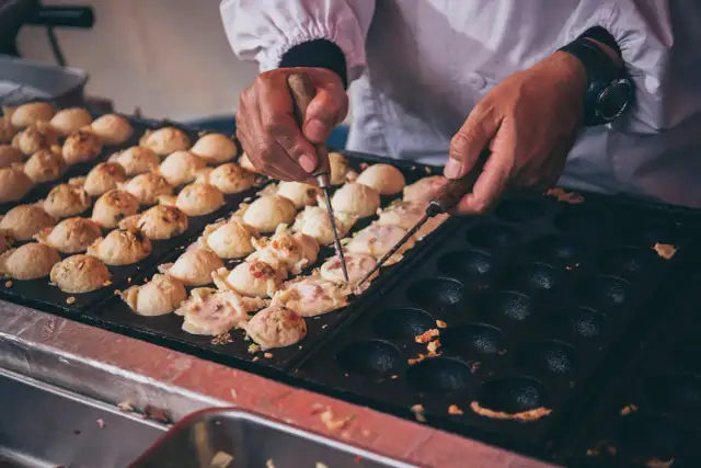 Ręce obracają kulki takoyaki na specjalnej patelni. Ten prosty takoyaki przepis jest w trakcie realizacji.
