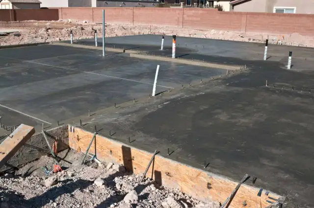 Świeży beton na fundamencie, przygotowany do dalszych prac, jak ocieplić fundament. Widoczne rury i zbrojenie.