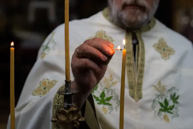 Dłoń duchownego zapala świecę podczas ceremonii.