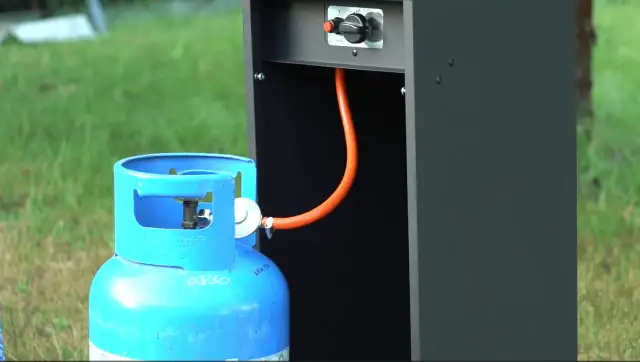 Niebieska butla z gazem LPG podłączona pomarańczowym wężem do czarnej obudowy.