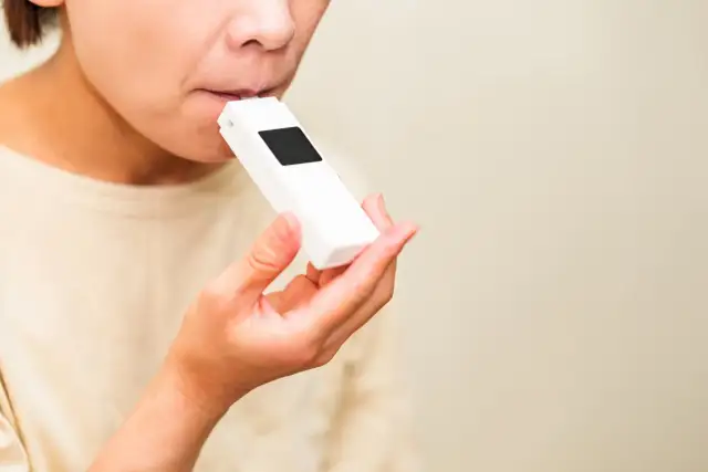 Osoba dmucha w biały alkomat trzymany w dłoni.