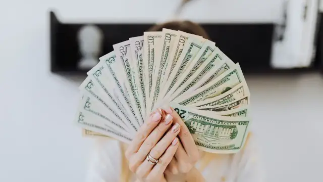 Dłonie trzymają wachlarz banknotów dolarowych.
