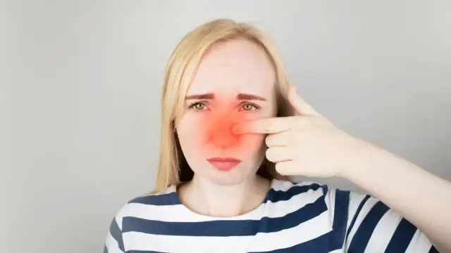 Kobieta z zaczerwienionym nosem, wskazująca palcem na ból. Szuka informacji, jak leczyć zatoki.