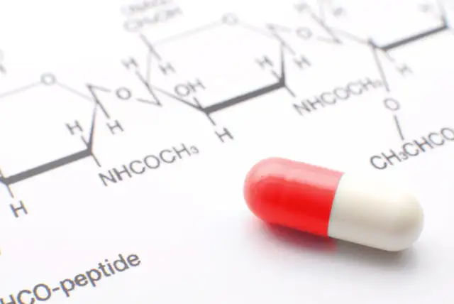 Kapsułka w kolorze czerwono-białym na tle schematu chemicznego.