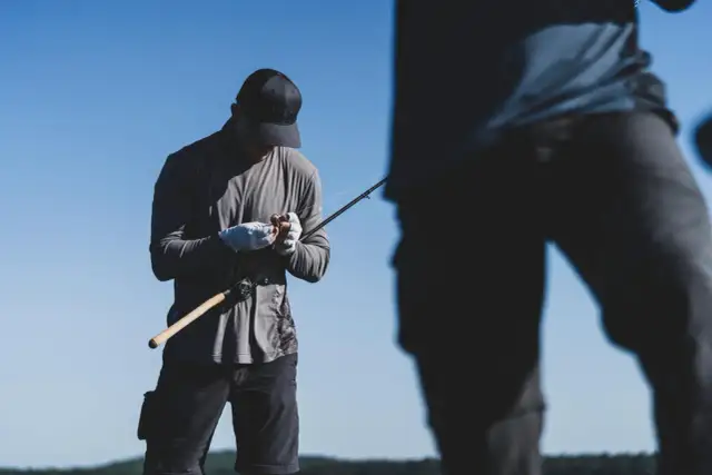 Wędkarz w białych rękawiczkach przygotowuje się do łowienia, pokazując, jak przymocować spławik do żyłki.