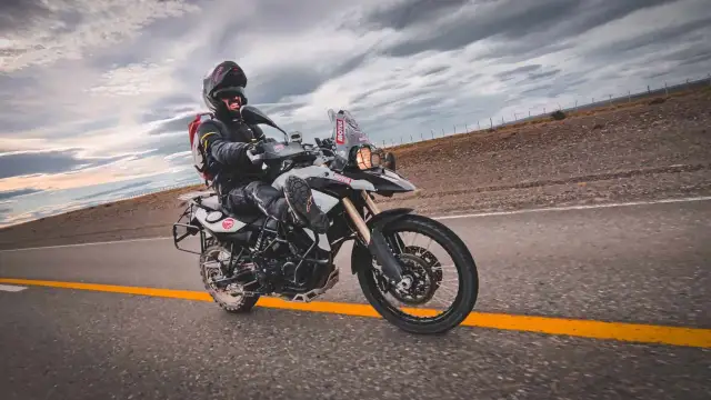 Motocyklista w kasku i kurtce pędzi na motocyklu BMW F 800 po pustej drodze pod burzowym niebem.