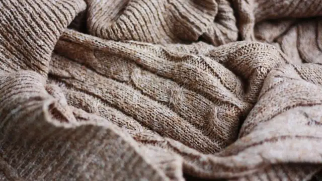 Zbliżenie na brązowy, wełniany sweter z warkoczowym splotem.