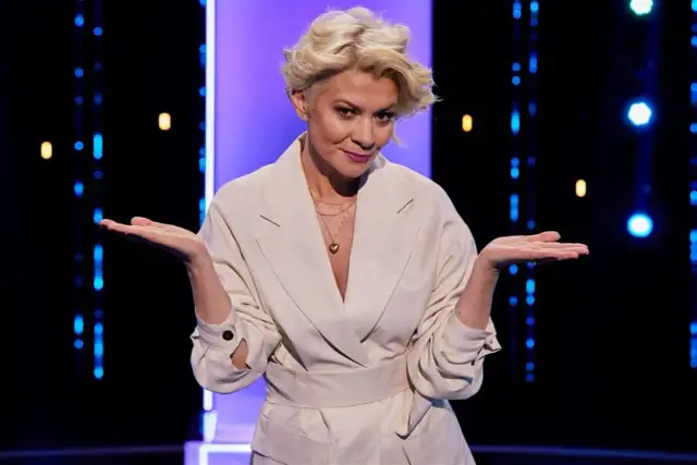 Kobieta w jasnym płaszczu z serduszkiem na szyi, gestykuluje. To może być zwiastun Magia nagości Polska sezon 1.