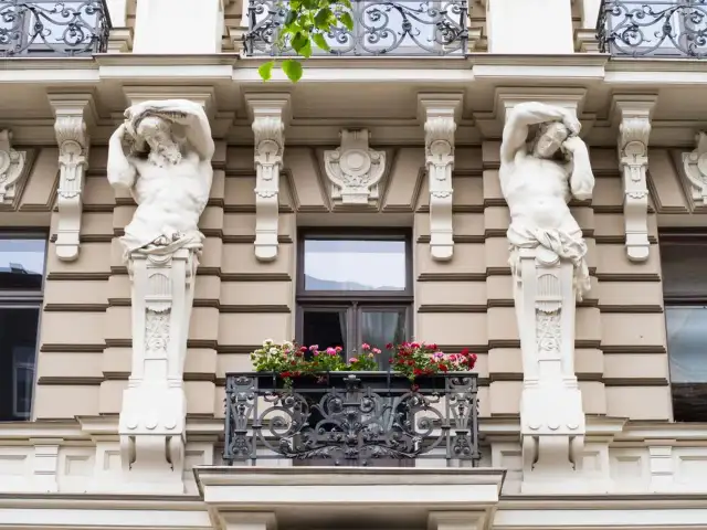 Dwie rzeźby atlantesów podtrzymują balkon w stylu secesyjnym. Kwiaty dodają koloru tej architekturze.