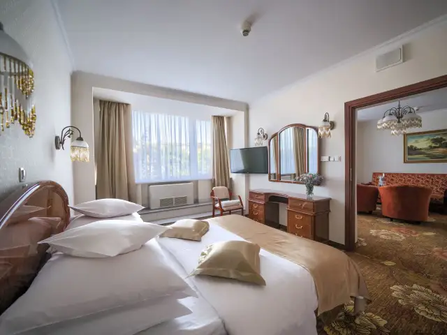 Elegancki pokój hotelowy z dużym łóżkiem, toaletką i widokiem na salon. Dowiedz się, ile kosztuje noc w hotelu Gołębiewski.