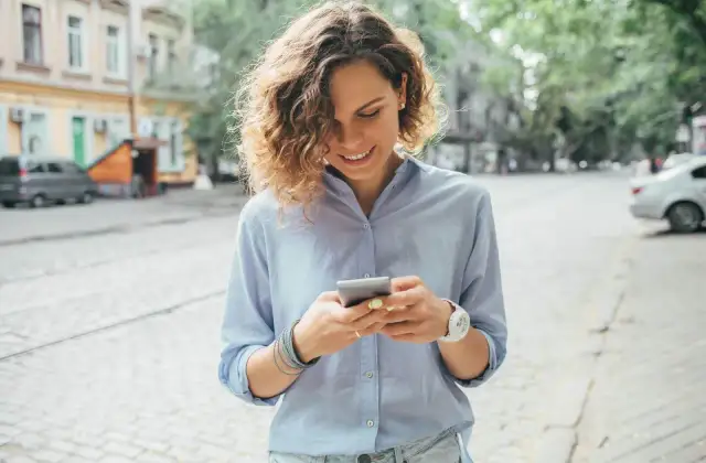Uśmiechnięta kobieta na ulicy sprawdza telefon, być może szuka informacji o pożyczka kontomatik.