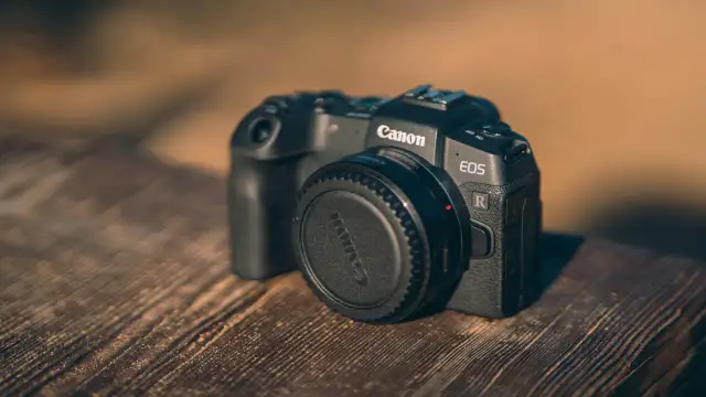 Czarny aparat Canon EOS R z zaślepką na obiektyw na drewnianym stole.