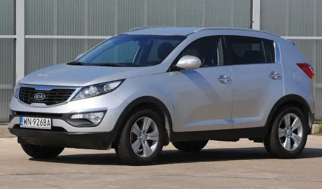 Srebrny Kia Sportage, jeden z najmniej awaryjnych aut terenowych, zaparkowany przed budynkiem.