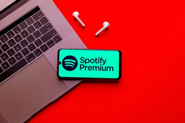 Telefon z logo Spotify Premium na tle laptopa i słuchawek bezprzewodowych.
