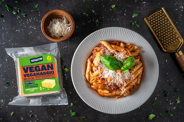 Talerz penne z sosem, opakowanie wegańskiego parmezanu i złota tarka.