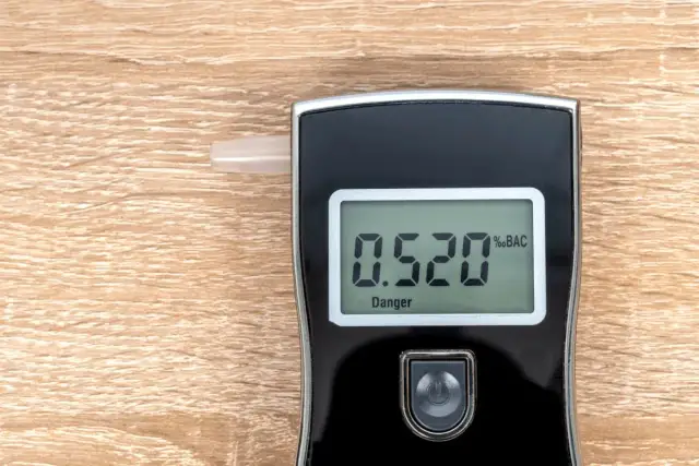 Alkomat z wyświetlaczem pokazującym 0.520 %BAC i napisem "Danger" na drewnianym tle.