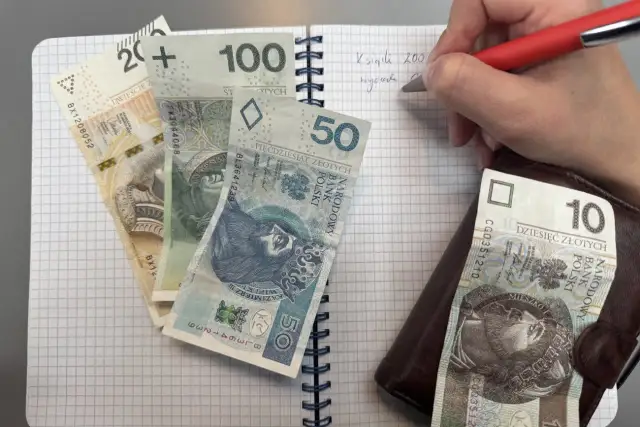 Zapisywanie wydatków na dziecko z orzeczeniem o potrzebie kształcenia specjalnego. Na zeszycie leżą banknoty 200, 100, 50 i 10 zł.