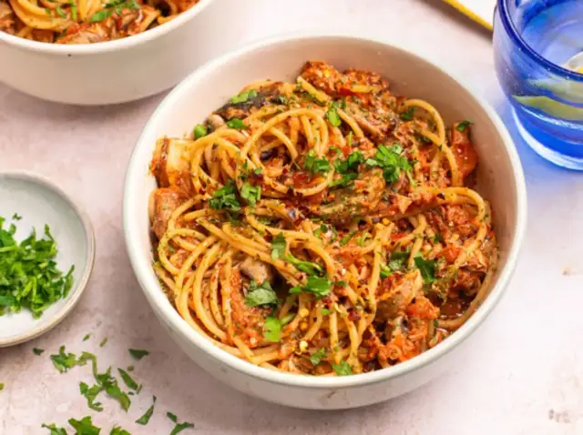 Miseczka spaghetti z sosem pomidorowym, grzybami i posiekaną natką pietruszki.
