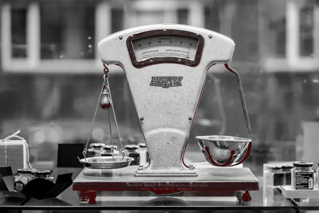 Stara waga szalkowa Avery z miseczkami i wagą na tle rozmytego okna.