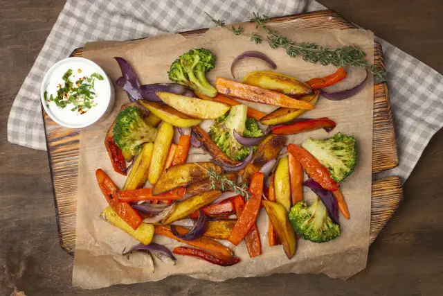 Pieczone warzywa: marchewka, ziemniaki, brokuły i cebula z sosem.