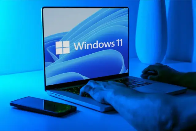 Ręce na klawiaturze laptopa z logo Windows 11. Dowiedz się, jak wejść do BIOS-u Windows 11, aby dostosować ustawienia.
