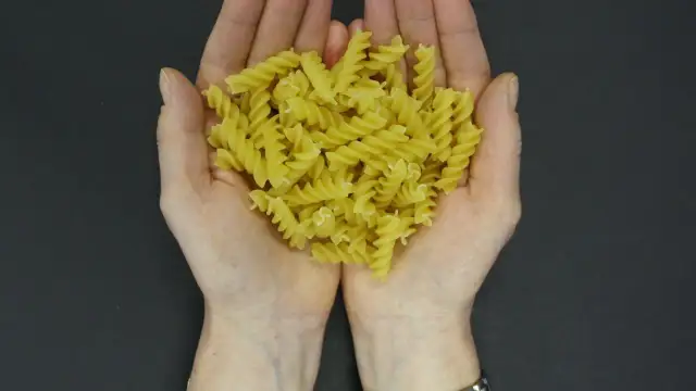 Dłonie trzymające porcję żółtego makaronu fusilli na ciemnym tle.