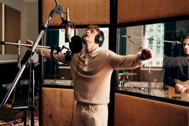 Mann mit Kopfhörern singt in ein Mikrofon, im Hintergrund spielt ein Mann Gitarre.