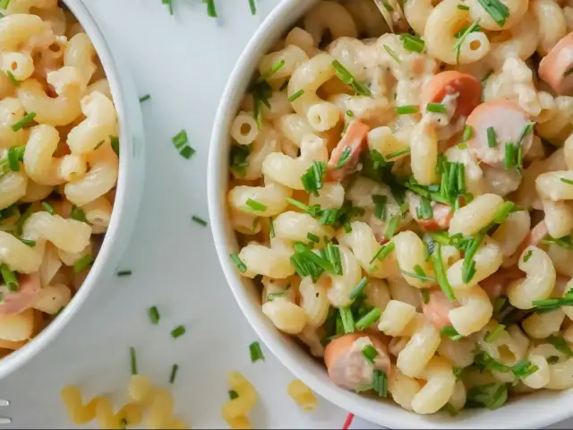 Makaron z parówkami i szczypiorkiem w kremowym sosie, podany w białej misce.